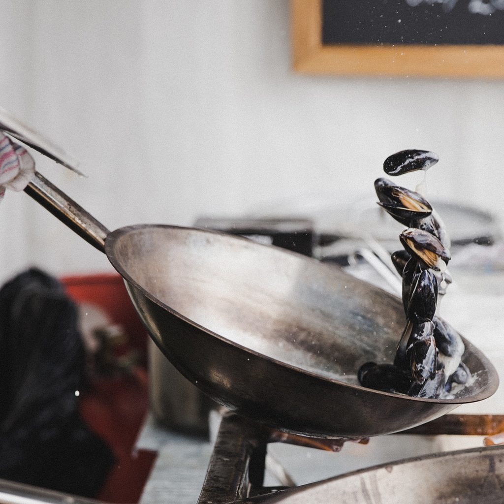 Person tossing clams in stainless steel pan