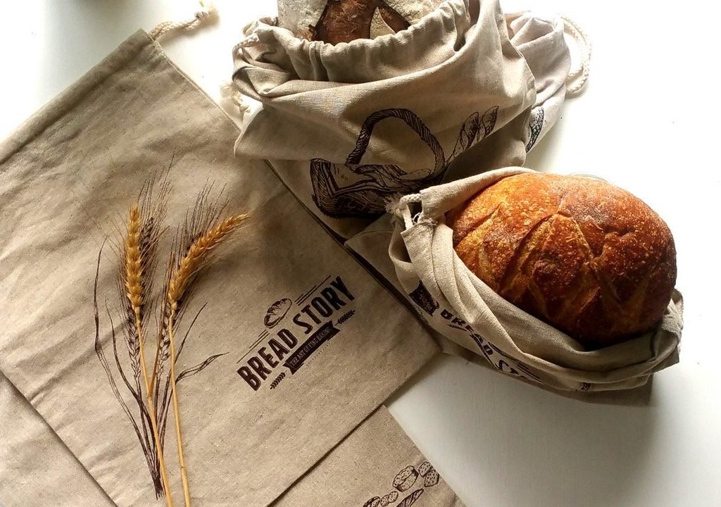 Loaf of bread and empty Bread Story Natural Linen Bread Bags on white countertop