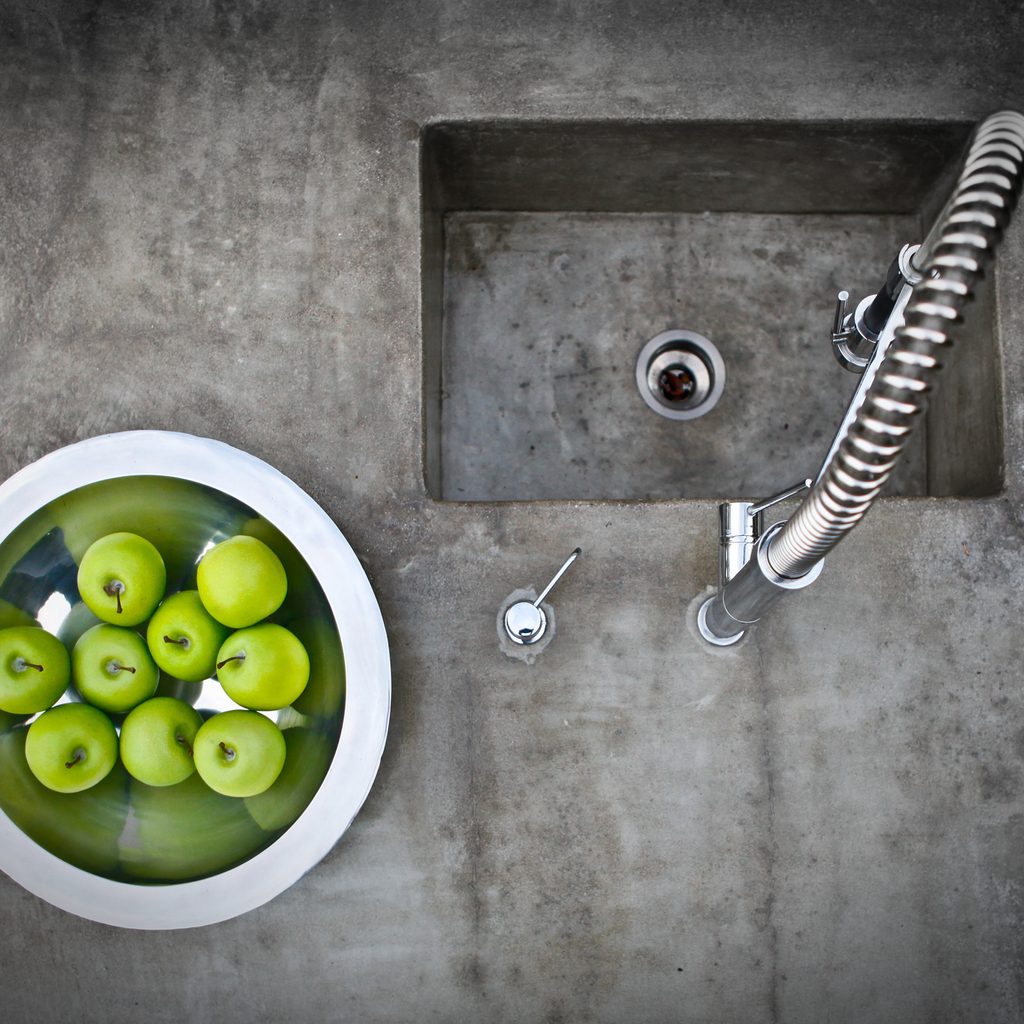 Concrete counter and sink with metal bowl of green apples