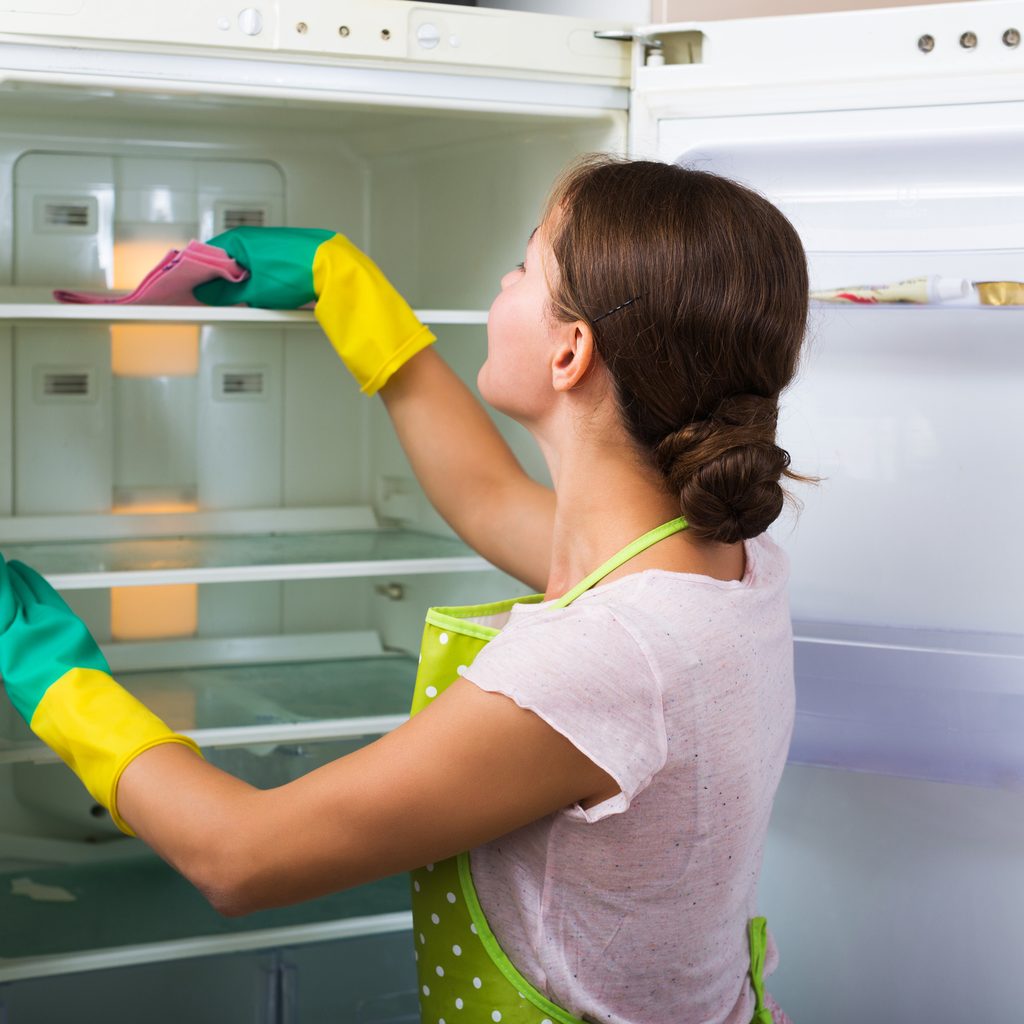 Woman in yellow gloves cleaning refrigerator