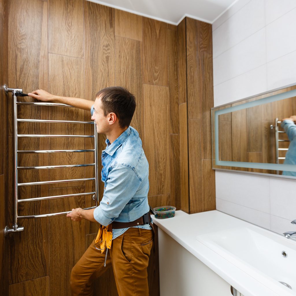 Person installing towel warmer rack on wall in bathroom.