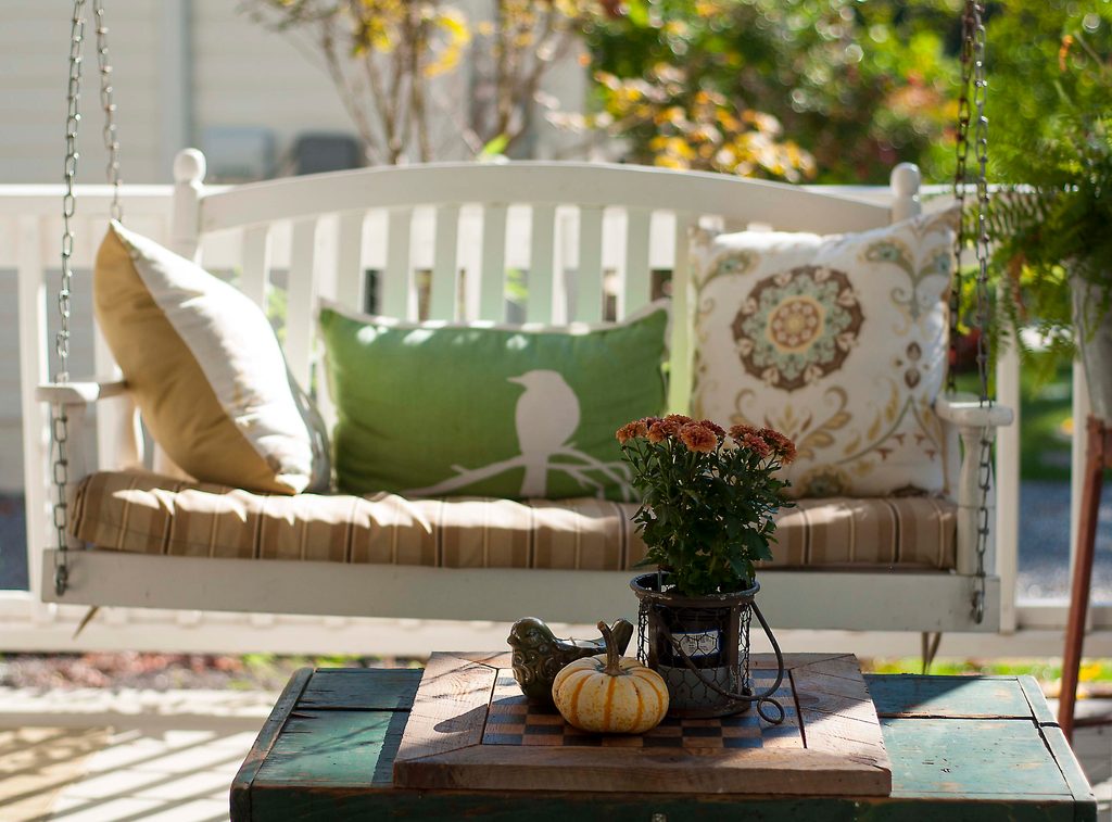 porch swing with pillows on it and small table in front