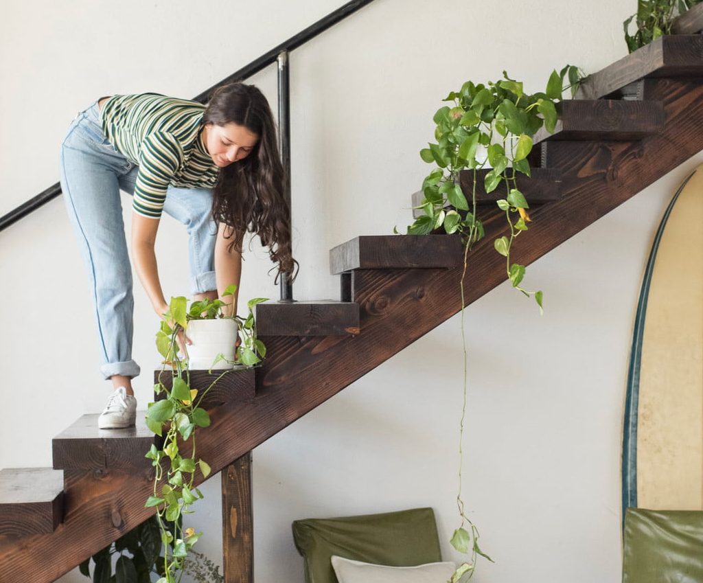Young woman on stairs in a loft caring for potted plants.