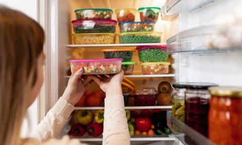 Woman standing in front of refrigerator filled with storage containers of food