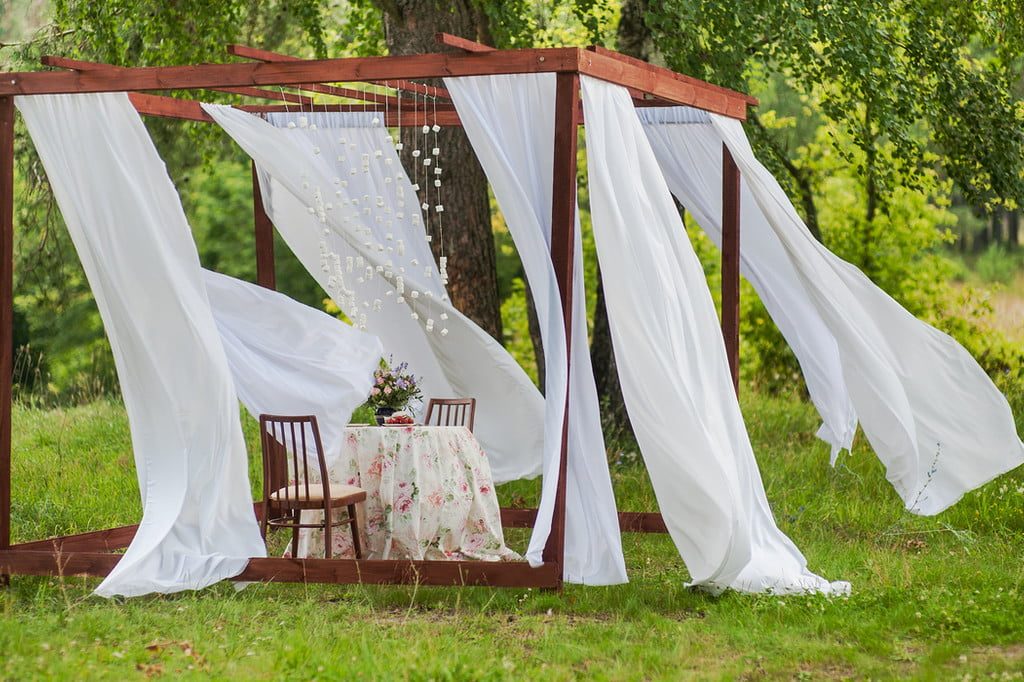gazebo pergola with small sitting area and white flowing curtains