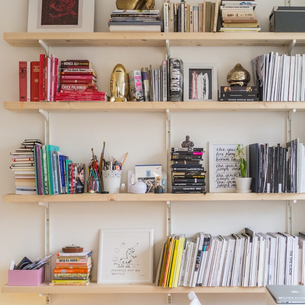 A light wooden bookshelves climb a white wall