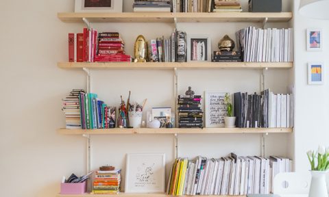 A light wooden bookshelves climb a white wall.