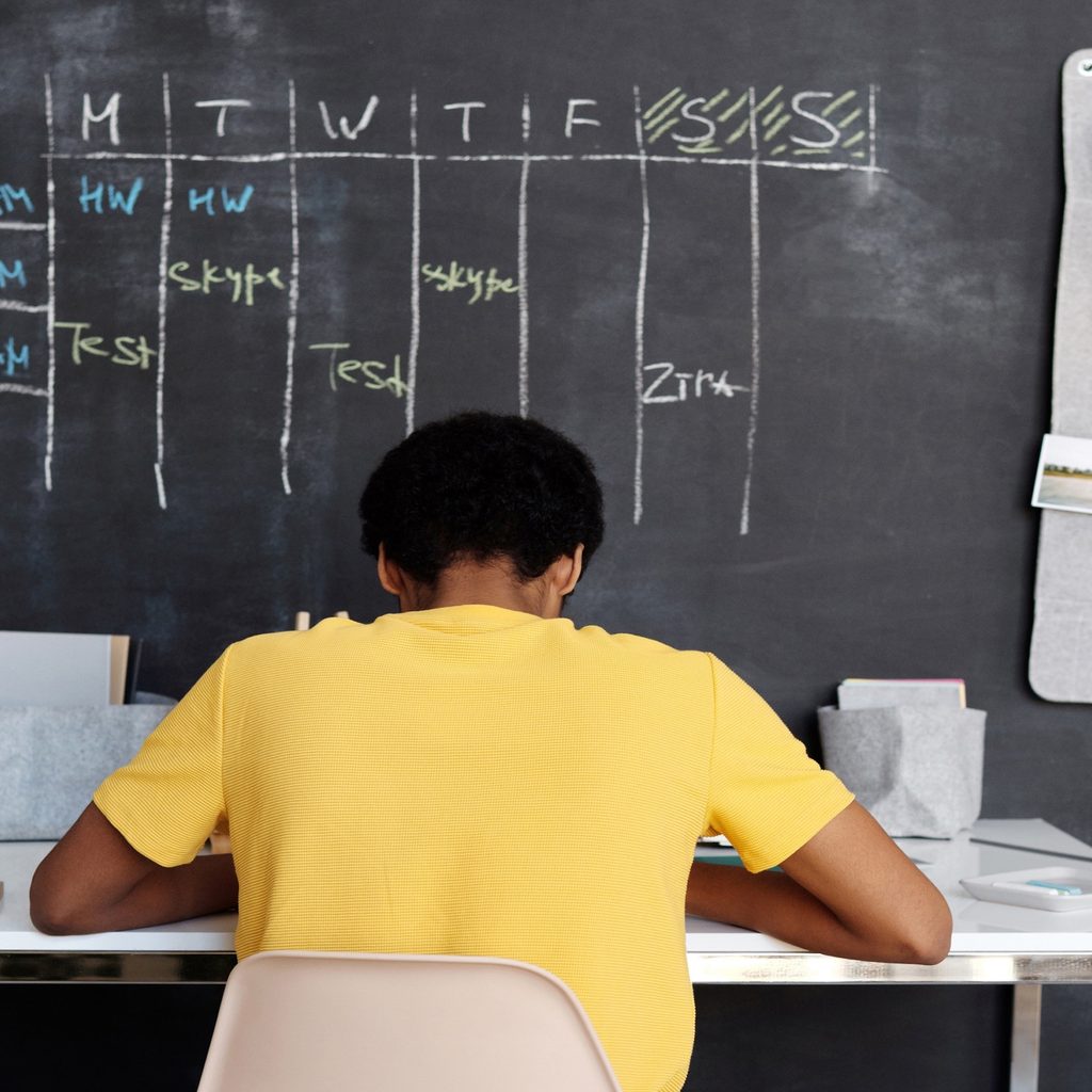 A young boy in a yellow shirt studies at a desk placed in front of a black chalkboard wall