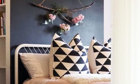 Flowers hang on a statement wall above a white-framed bed with navy blue and white pillows