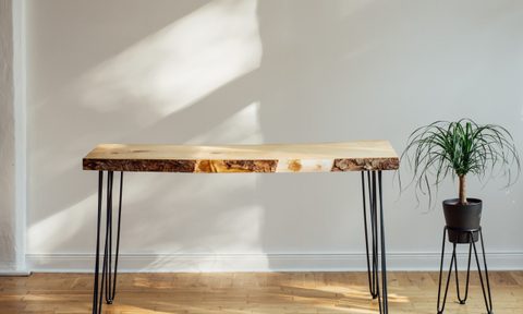 A wooden table sits on a light wood floor in front of a white wall.