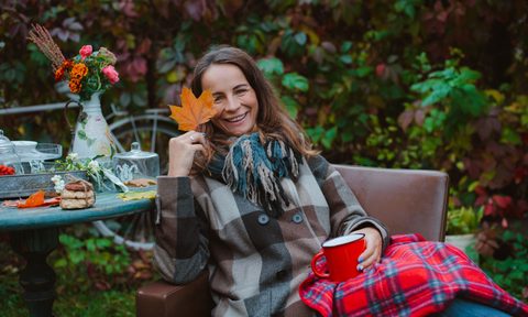 Woman on patio holding a leaf and mug with checkered blanket on lap