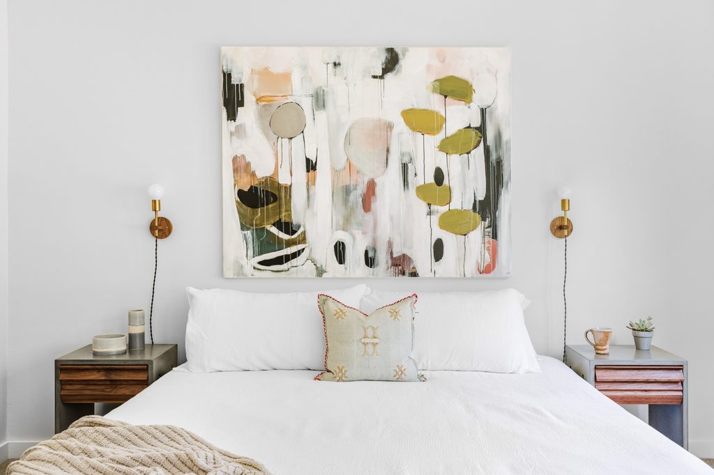 A green and brown abstract painting of leaves hangs above a bed.