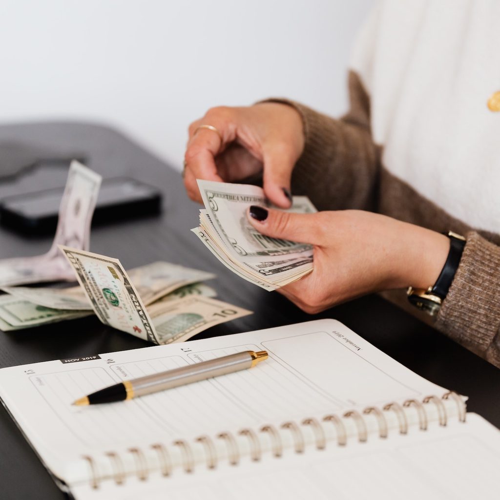 woman counting money next to notebook