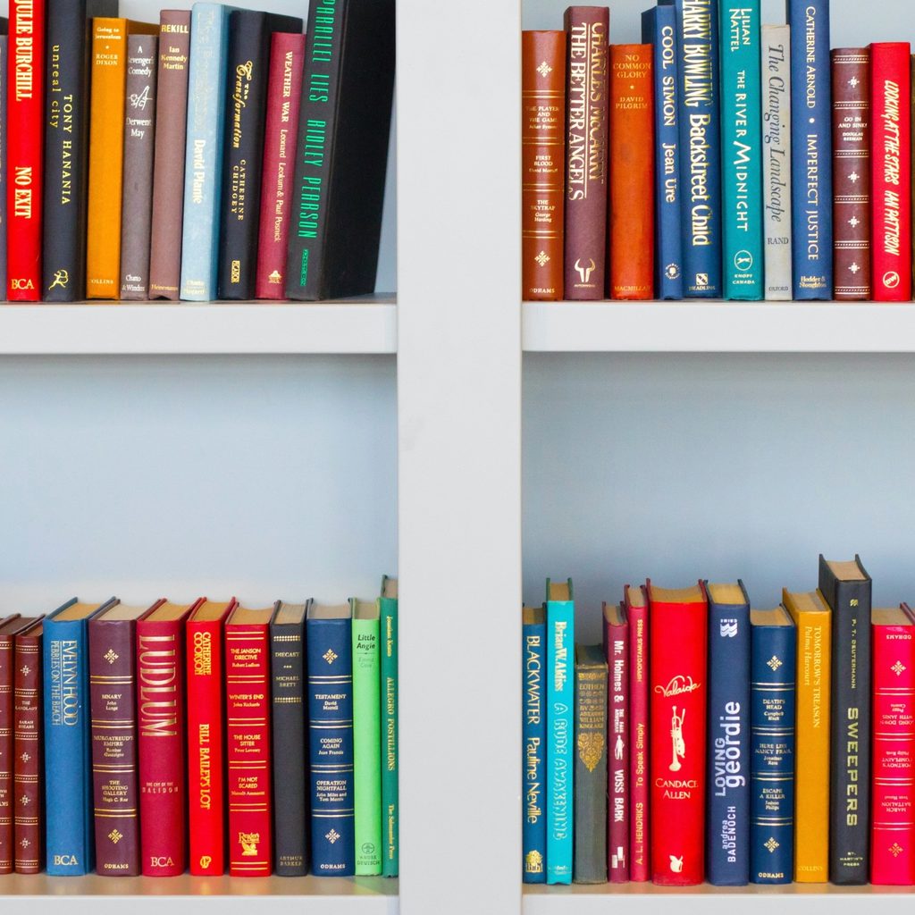 Books of all different colors are stacked on a set of white bookshelves.