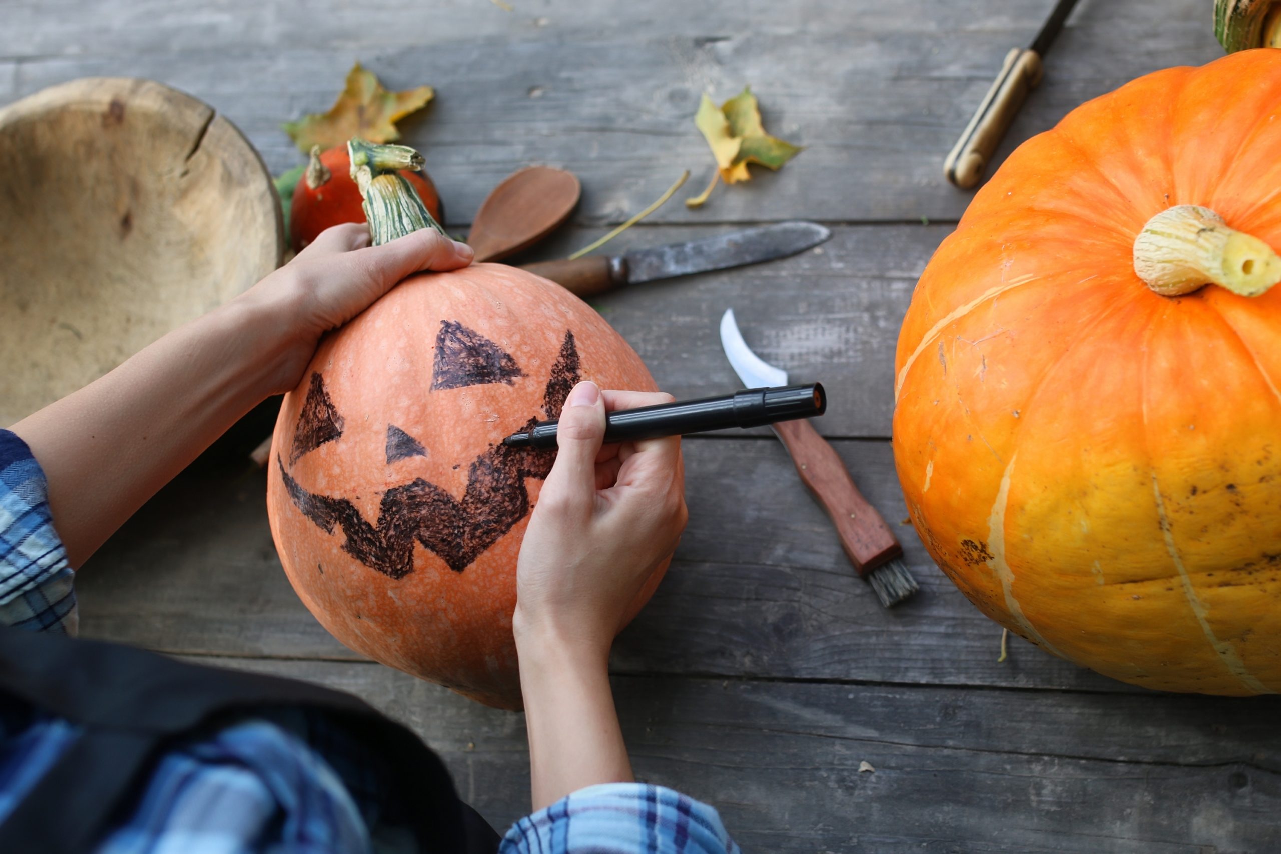 person drawing with sharpie on a pumpkin