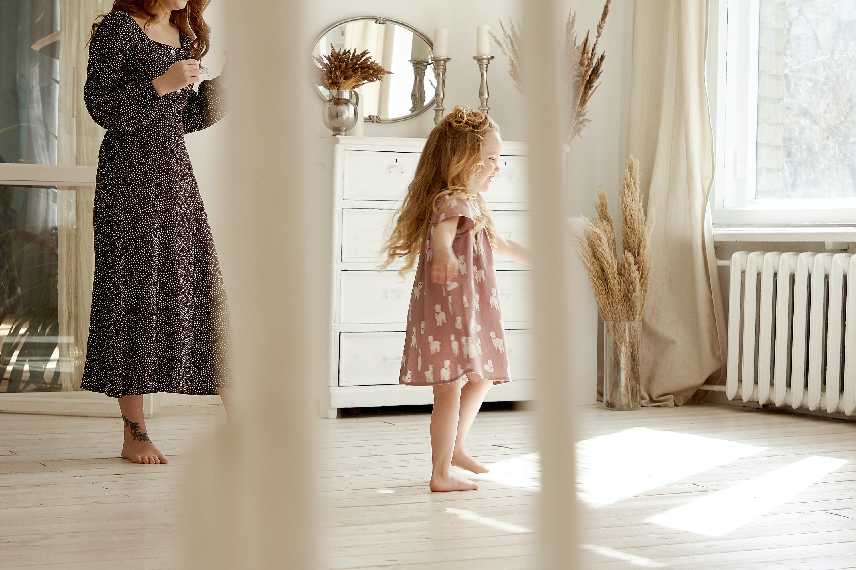 Woman standing behind toddler in sunny room