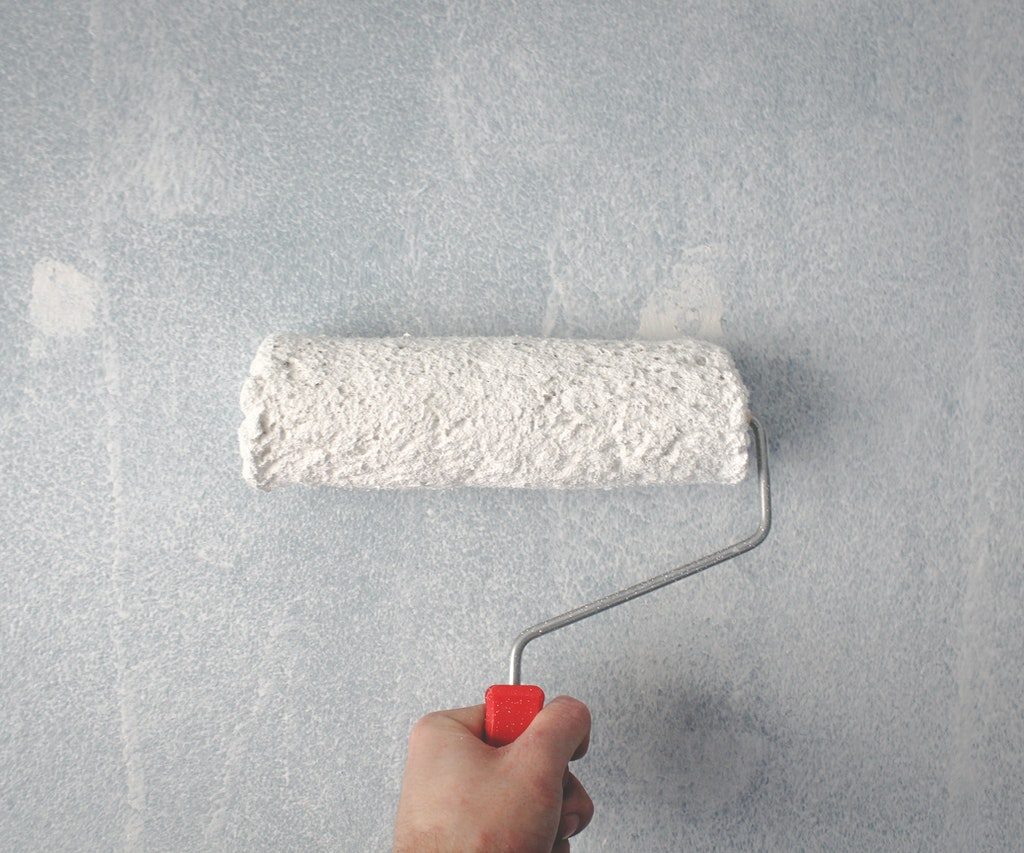 Hand holding paint roller against white wall
