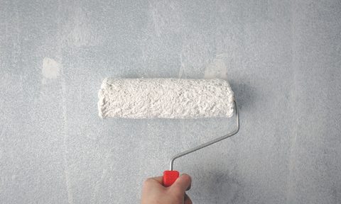 Hand holding paint roller against white wall