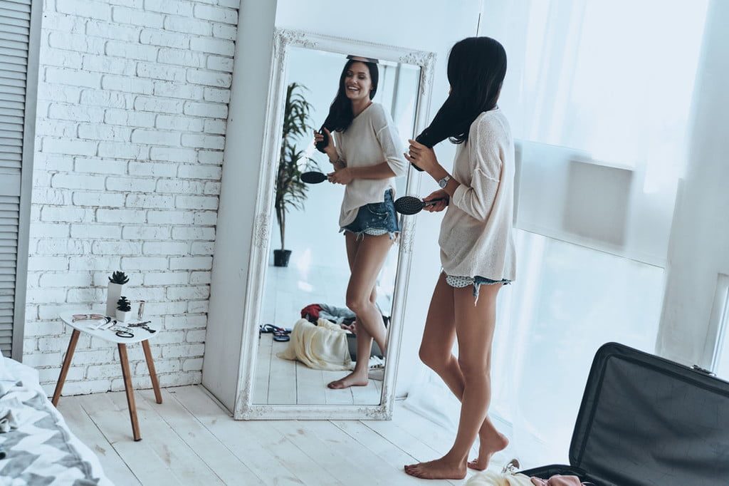 Young woman brushing hair in front of full length mirror