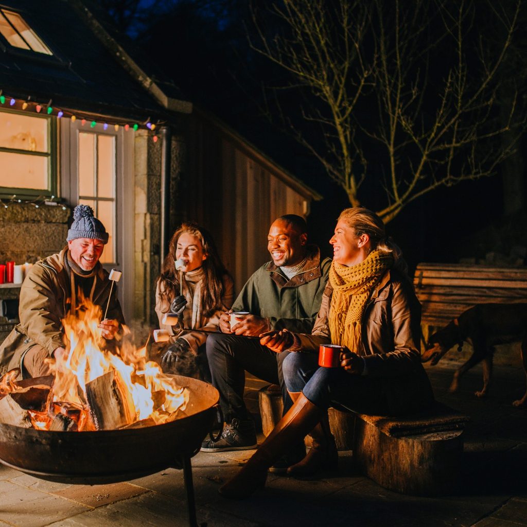 Two couples using a backyard firepit at night