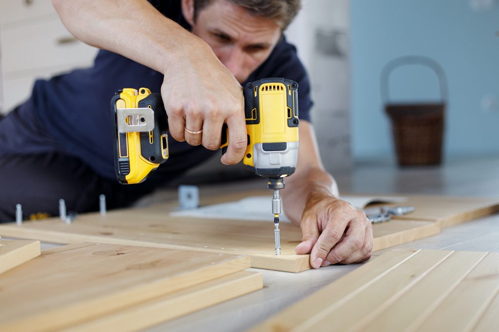 man using an electric drill on a screw in wood