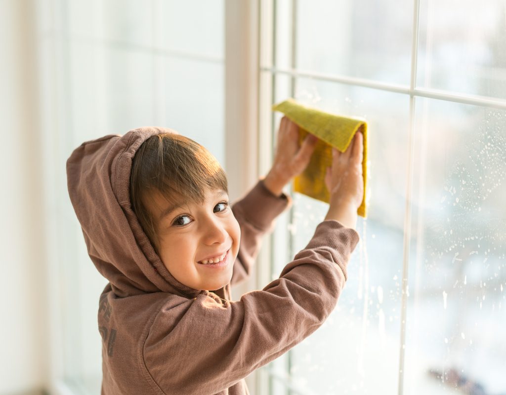 A young boy washing windows with a cloth