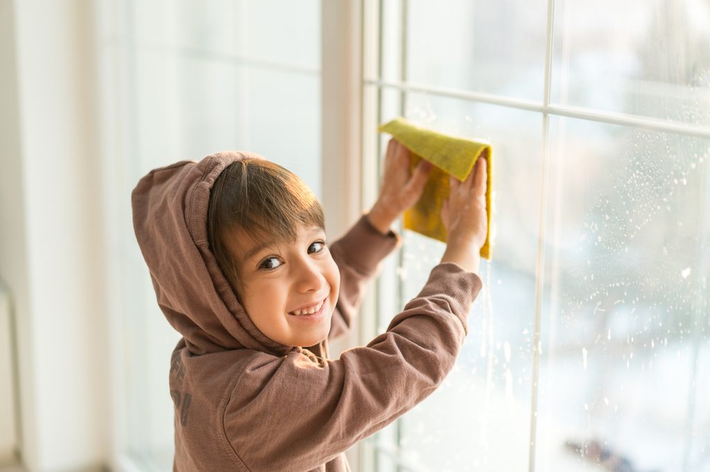 A young boy washing windows with a cloth