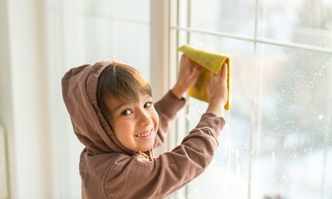 A young boy washing windows with a cloth