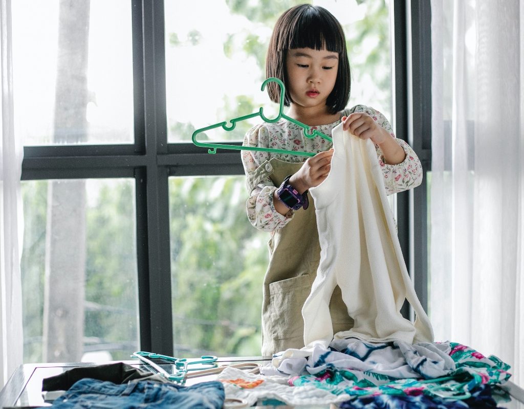 young girl hanging dress with a pile of laundry