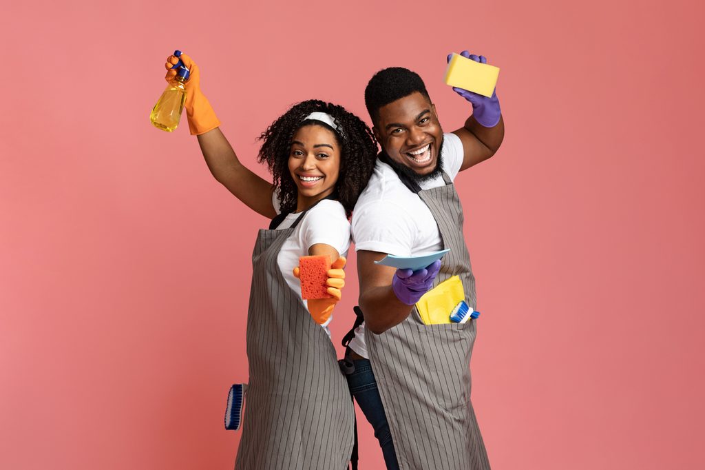 Man and woman in overalls smiling with sponges and cleaning products