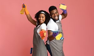 Man and woman in overalls smiling with sponges and cleaning products