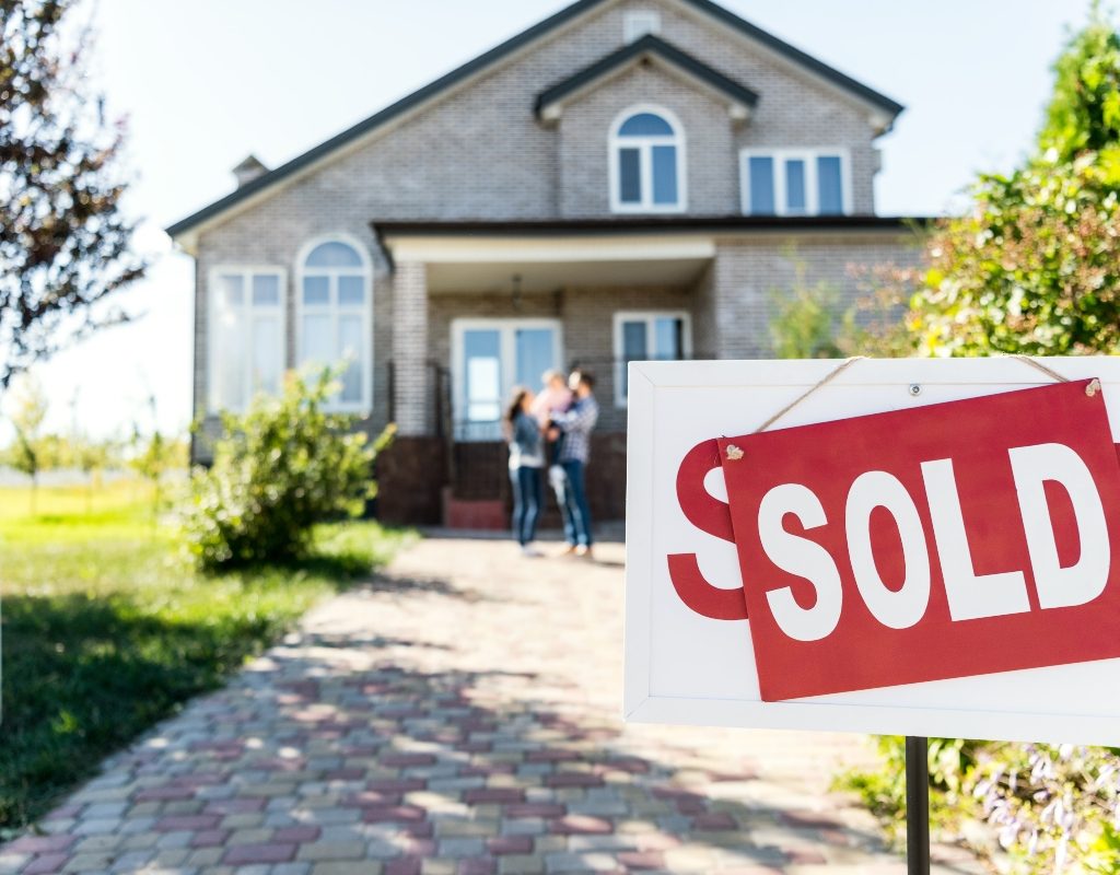 family in front of home with sold sign in yard