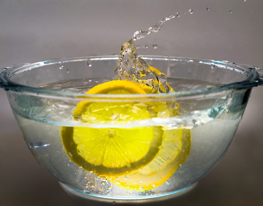 Lemon slices splashing in a glass bowl of water