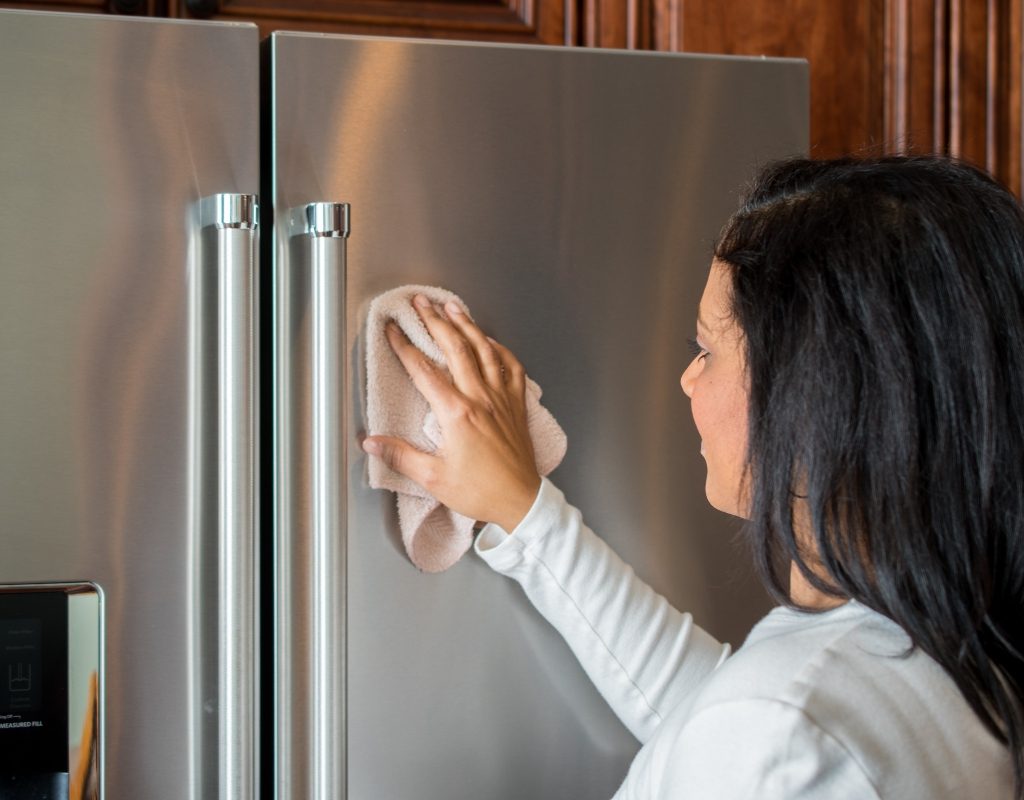 woman cleaning stainless steel fridge with vinegar