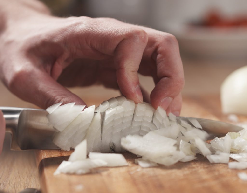 man dicing an onion on a cutting board