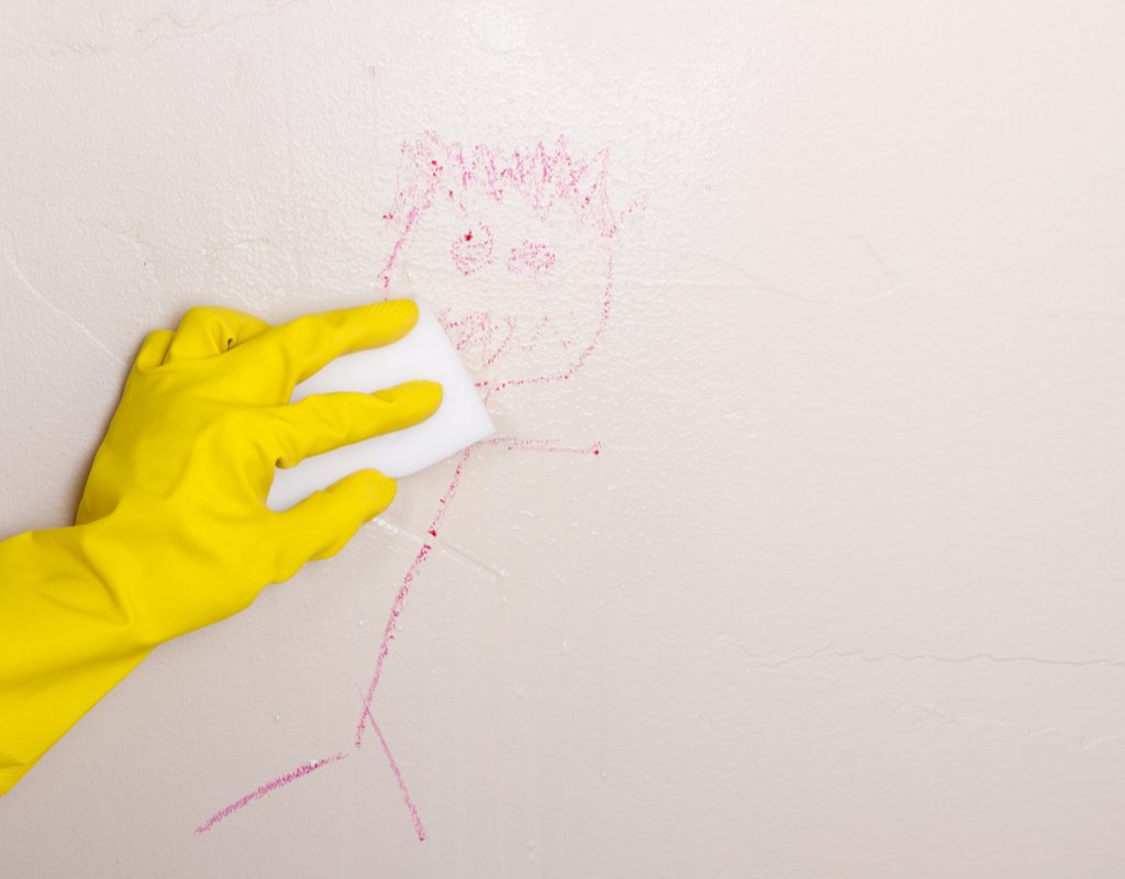 Gloved hand cleaning crayon off wall with a Magic Eraser