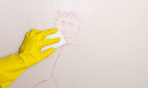 Gloved hand cleaning crayon off wall with a Magic Eraser