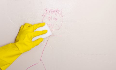 Gloved hand cleaning crayon off wall with a Magic Eraser