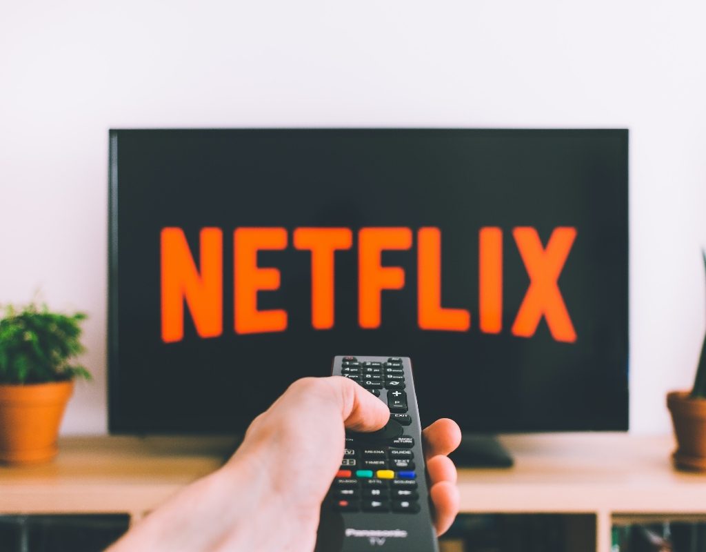 person holding remote towards tv displaying netflix logo