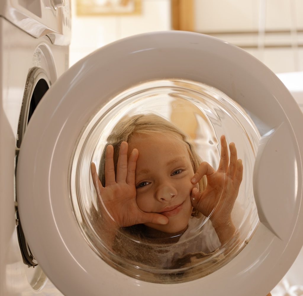 A little kid peaking behind the washer door.