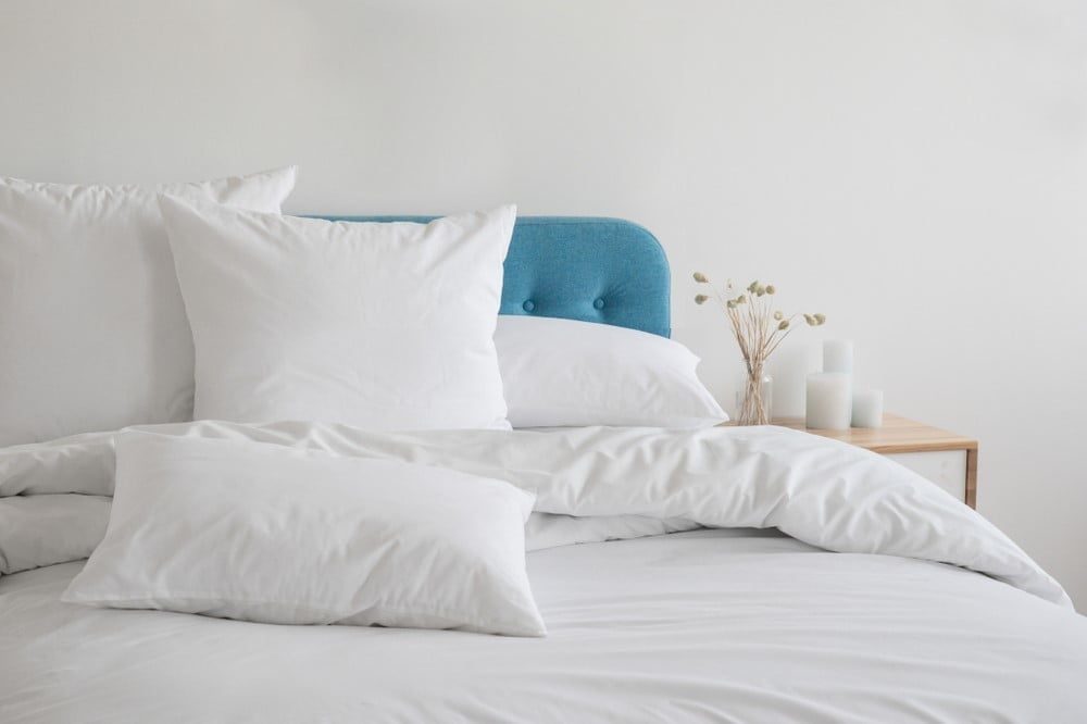 White pillows and comforter against a teal colored head board