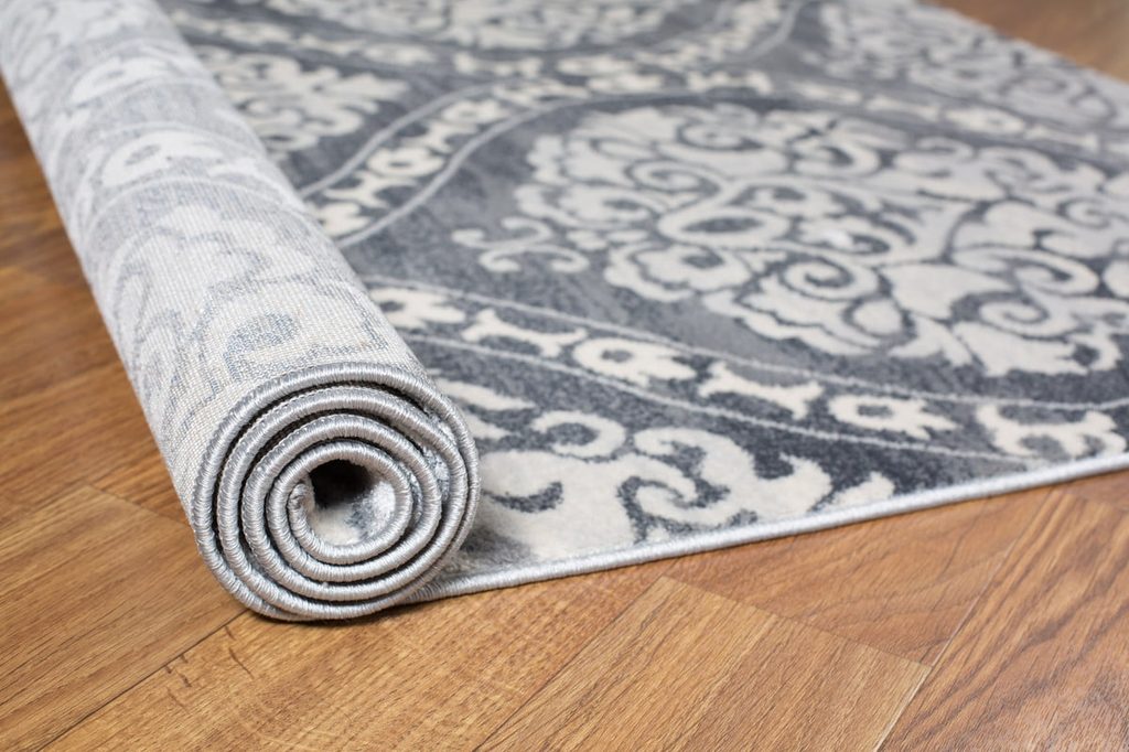 gray patterned rug being rolled out onto wood floor