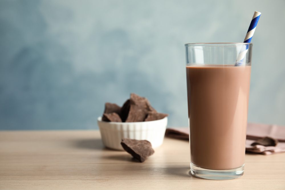 Tall glass of chocolate milk on wooden table near bowl of chocolate