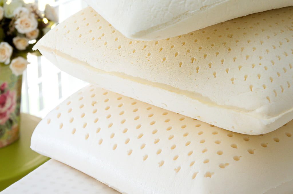Three natural latex pillows stacked on bed with flowers in background