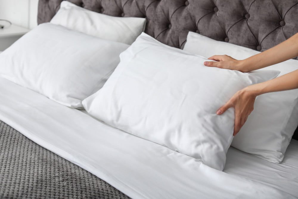 person placing white pillows on bed with gray comforter