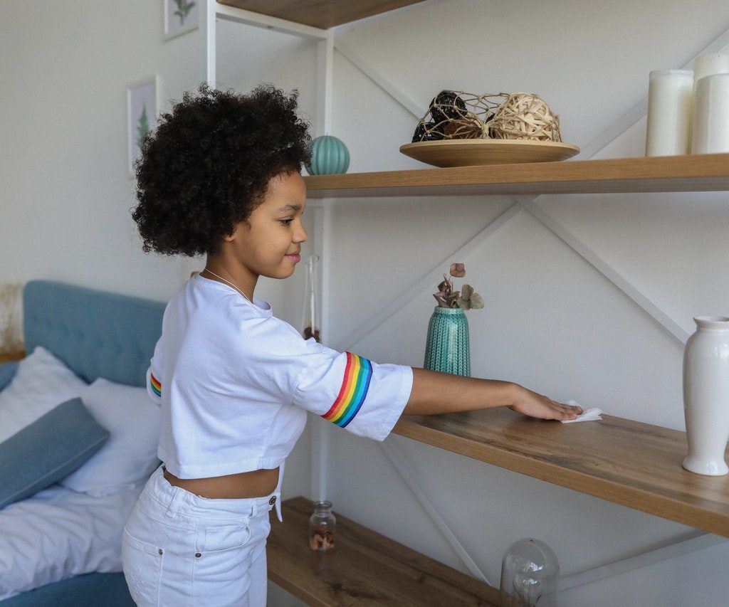 young girl dusting a shelf