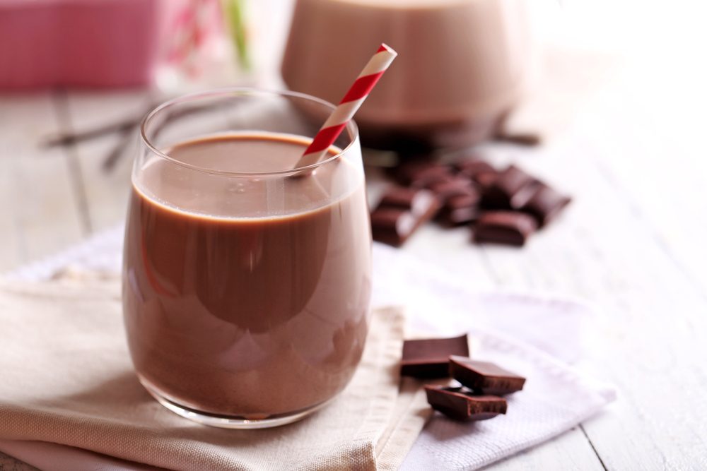 glass of chocolate milk with red and white straw on table near chocolate pieces