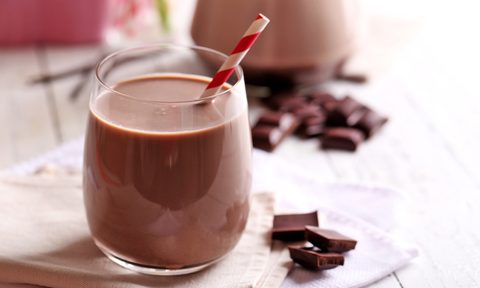 glass of chocolate milk with red and white straw on table near chocolate pieces