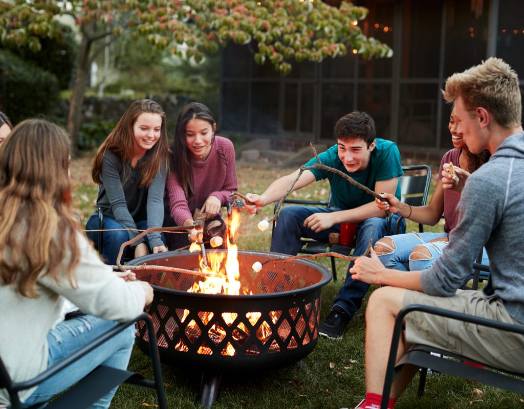 teenage friends toasting marshmallows around a fire pit