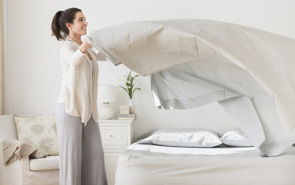 Woman putting white sheets on a bed